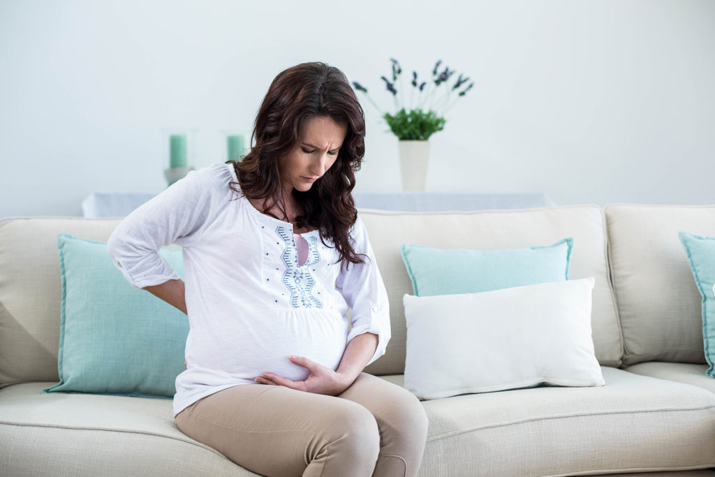 pregnant woman sitting on a couch holding her baby bump and back pain